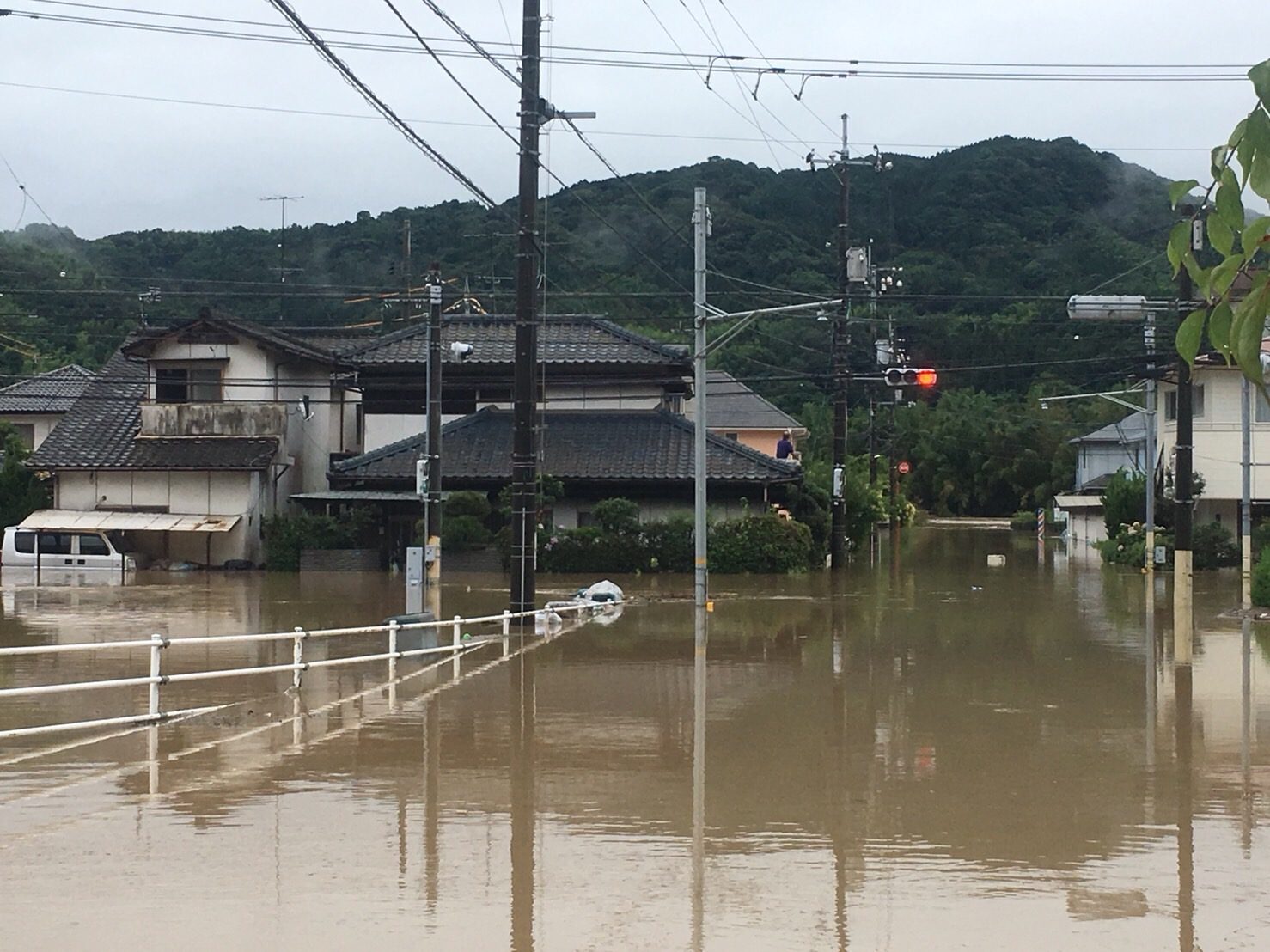 濁水に屋根近くまで沈んだ白いバンと、浸水した住宅街