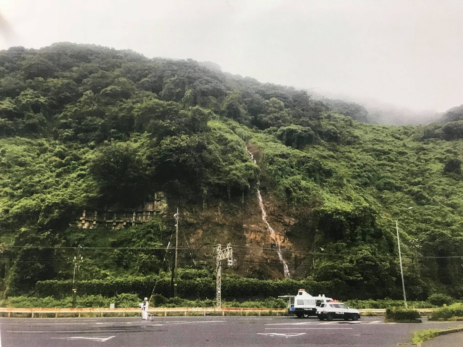 山腹が崩れた斜面の下で、警察車両が現場対応している様子