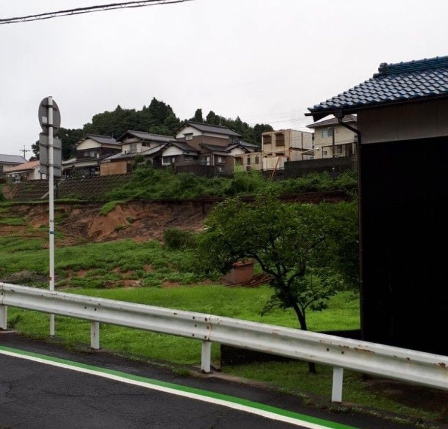 住宅の下の擁壁と斜面が崩れ、土が道路側に流れ出した現場
