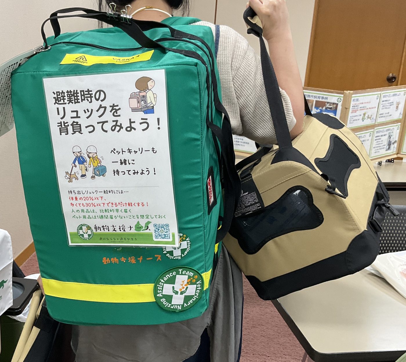 避難用リュックを背負い、ペットキャリーも持った実演。リュックには持ち出しの重さの目安が書かれている