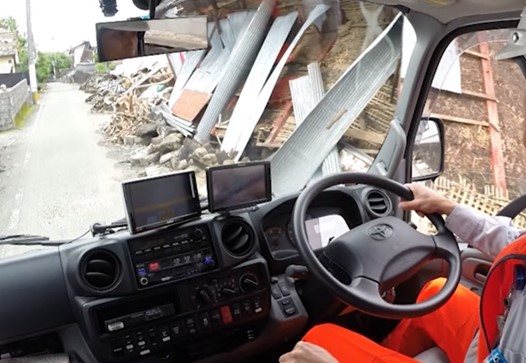 レッカー車の運転席から見た、瓦礫が道脇に積み上がった被災地の道路